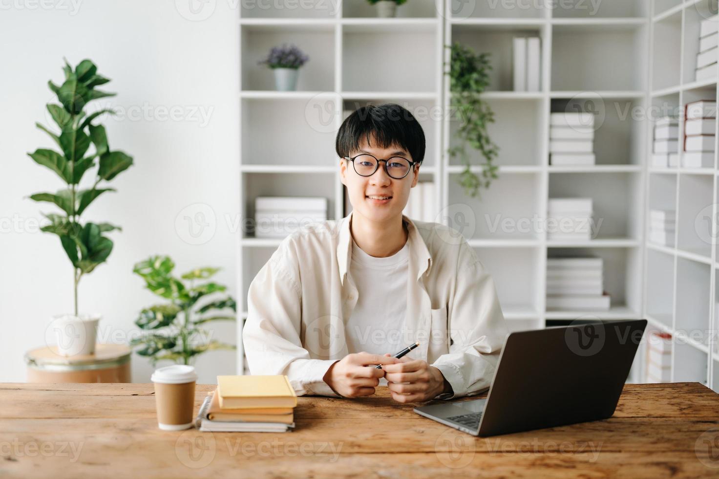 bonito e talentoso jovem ásia homem aluna trabalhando em dele projeto atribuição, usando computador portátil e tábua para procurar a conectados informações. foto