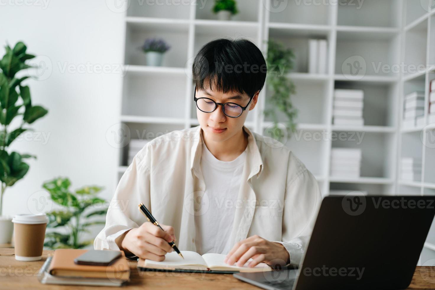 bonito e talentoso jovem ásia homem aluna trabalhando em dele projeto atribuição, usando computador portátil e tábua para procurar a conectados informações. foto