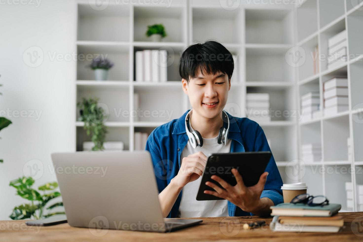 jovem atraente ásia homem sorridente pensando planejamento escrevendo dentro caderno, tábua e computador portátil trabalhando a partir de casa às casa escritório foto