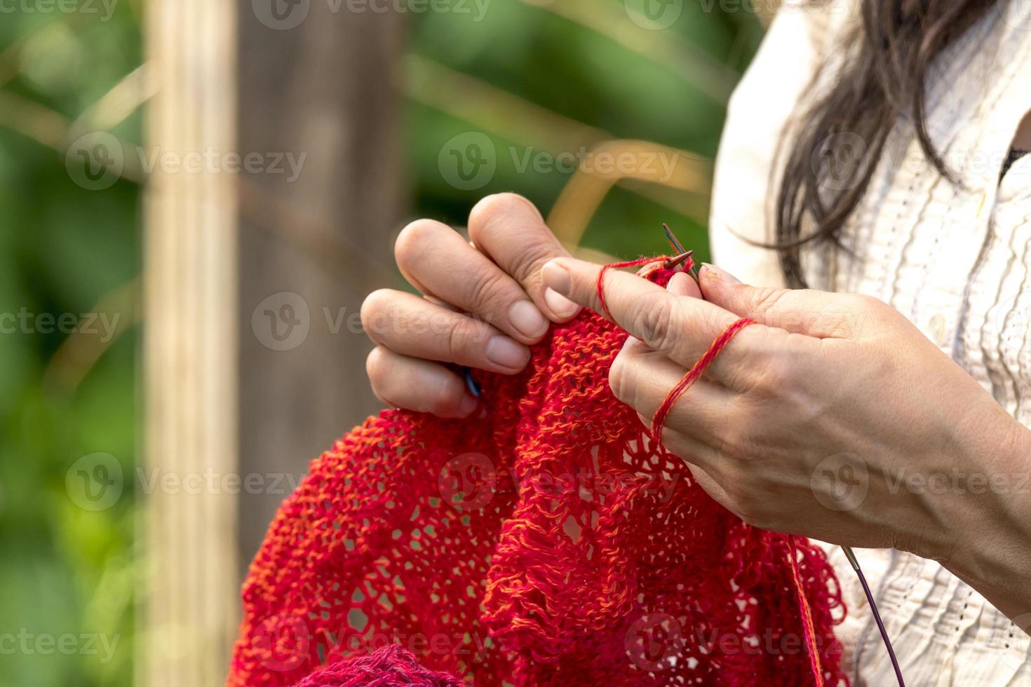 mãos de uma mulher que faz crochê com tricô de lã vermelha na frente do fundo desfocado foto