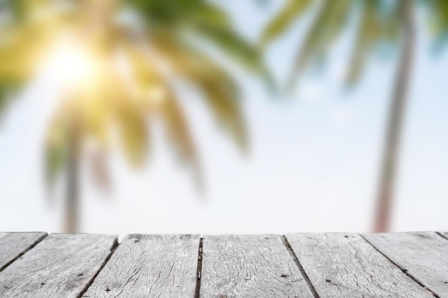 foco seletivo de mesa de madeira velha com uma bela praia embaçada com palmeiras tropicais para exibir seu produto. foto