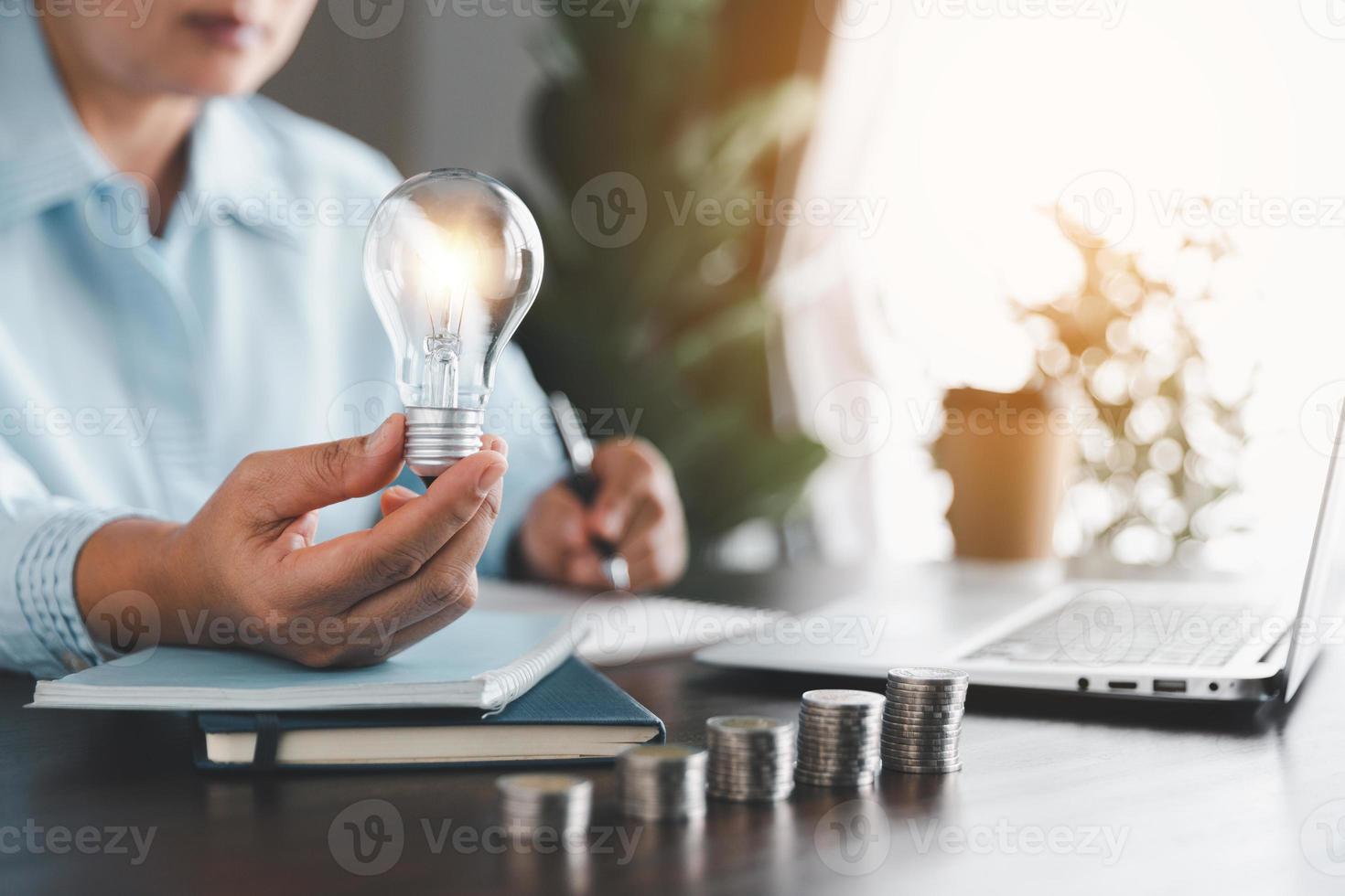 empresária mão segurando lâmpada com levar notas em a mesa. idéia do salvando energia e contabilidade finança dentro casa e família, Salve  mundo e energia poder. Salve  energia plano conceito. foto