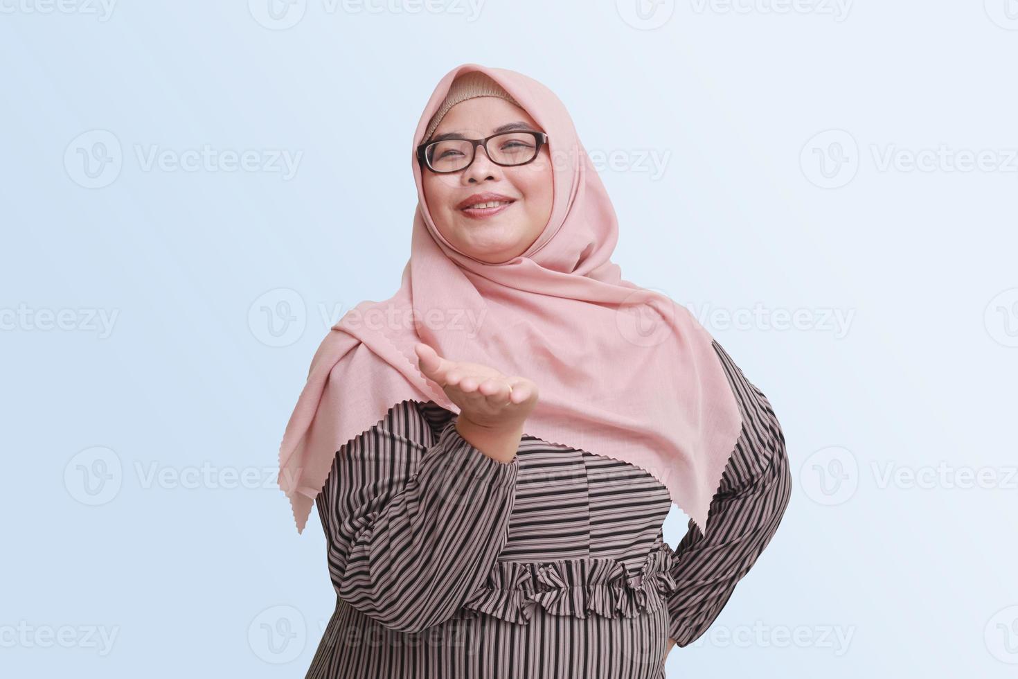 retrato do alegre ásia mulher com hijab, mostrando alguma coisa em esvaziar mão. publicidade conceito. isolado imagem em Rosa fundo foto