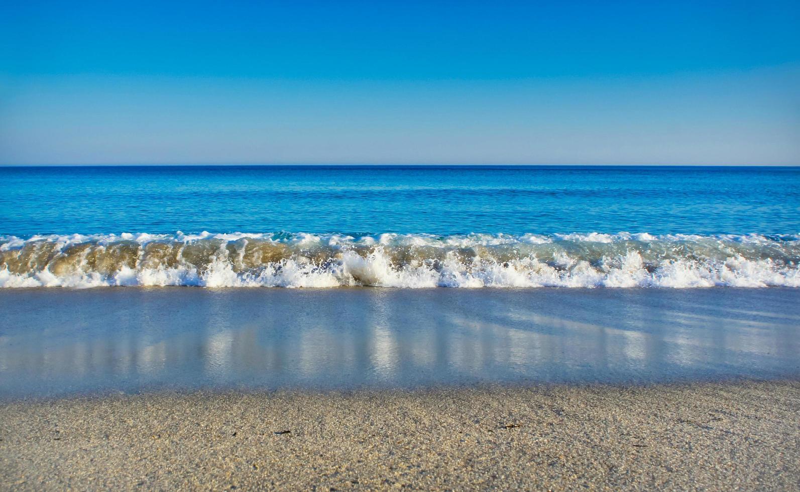 paisagem marinha com mar azul claro, céu sem nuvens e praia de areia branca foto