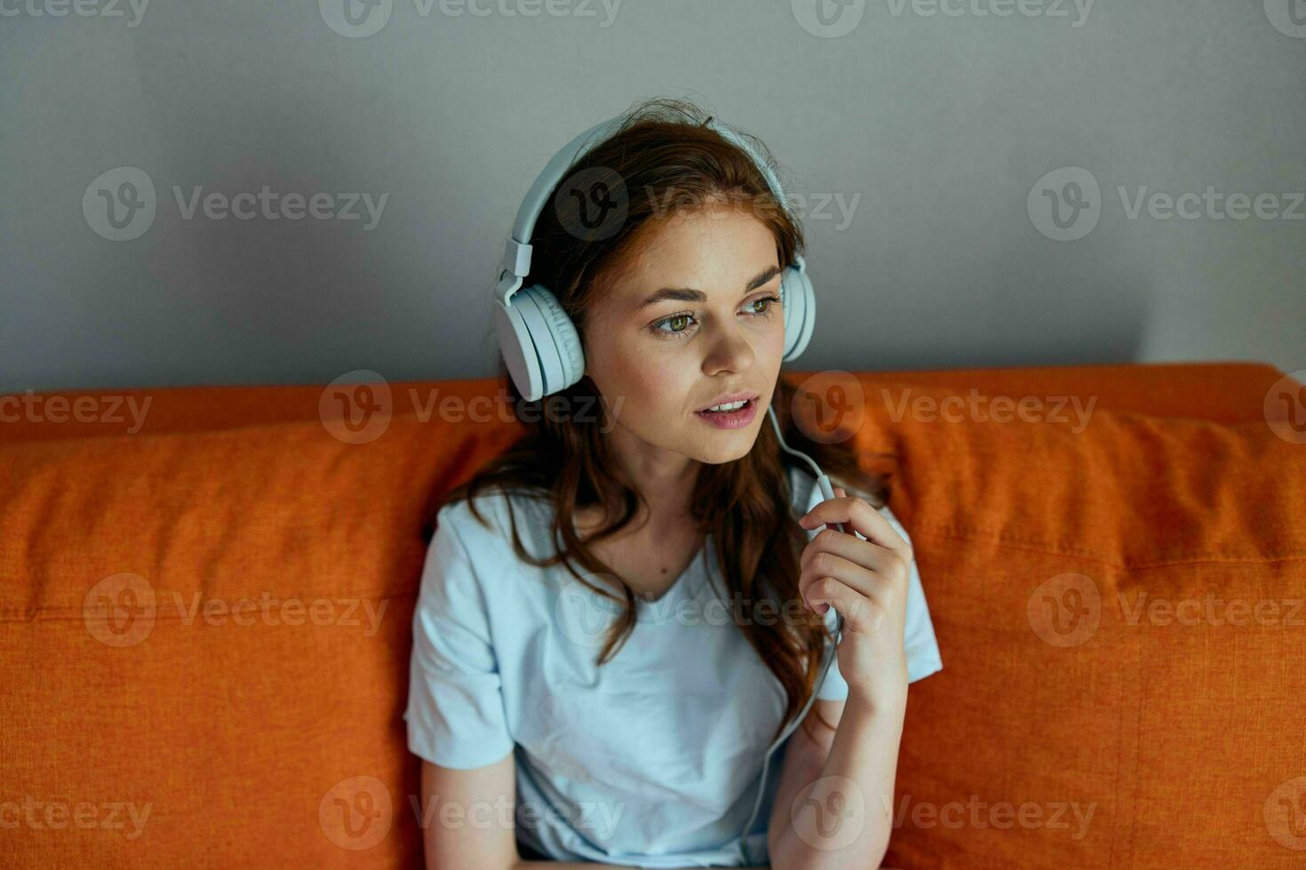 mulher em a laranja sofá ouvindo para música com fones de ouvido tecnologias foto