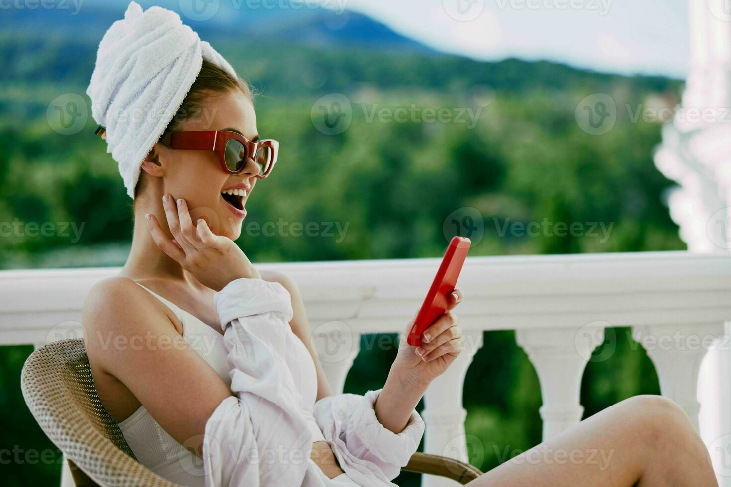 retrato do jovem mulher usando Móvel telefone enquanto sentado em sacada com uma lindo natureza Visão preguiçoso manhã foto