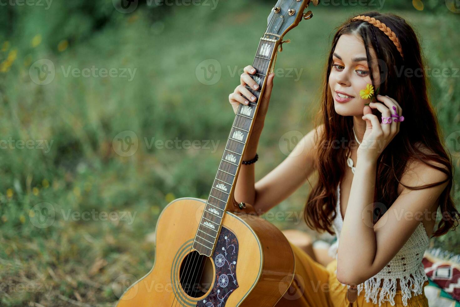 feliz hippie mulher com uma guitarra relaxante dentro natureza sentado em uma xadrez sorridente e desfrutando a visualizar. estilo de vida dentro harmonia com natureza e auto foto