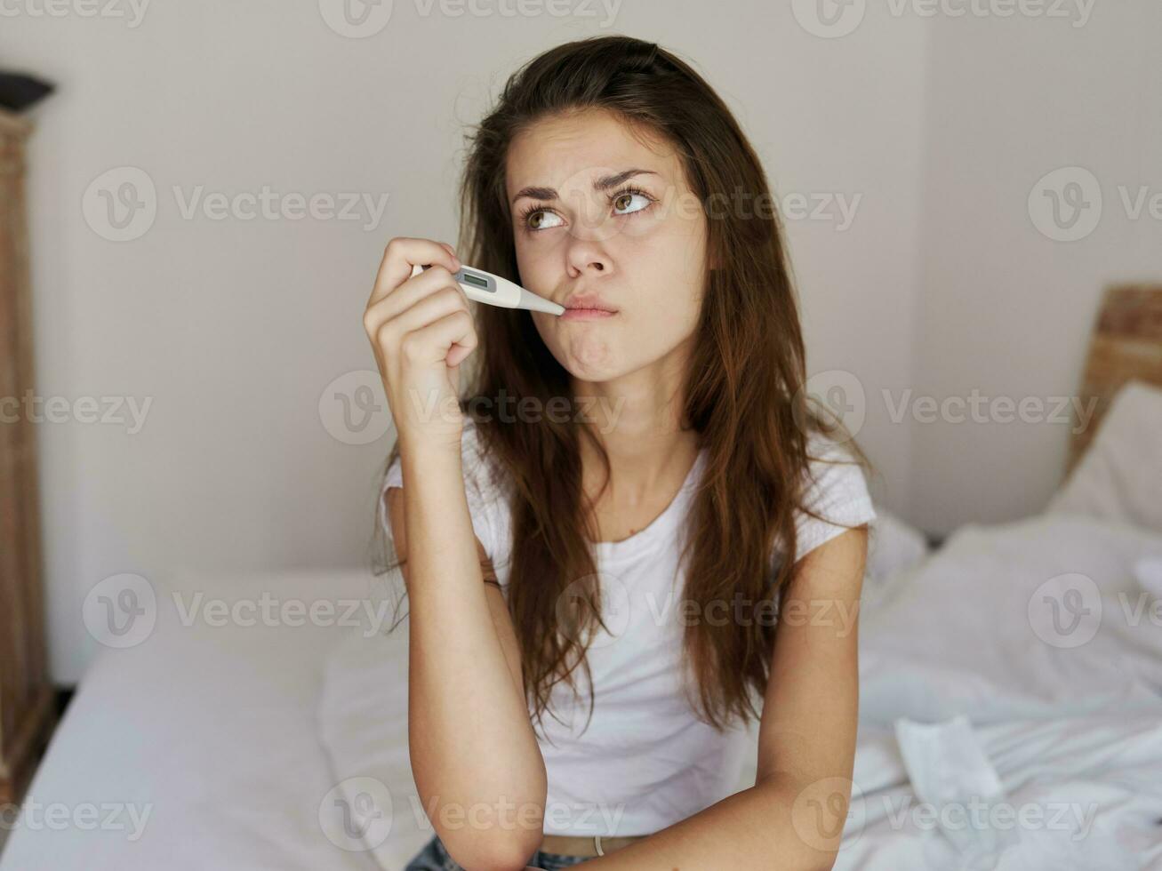 mulher esperando com uma termômetro dentro dela boca sentado em a cama foto