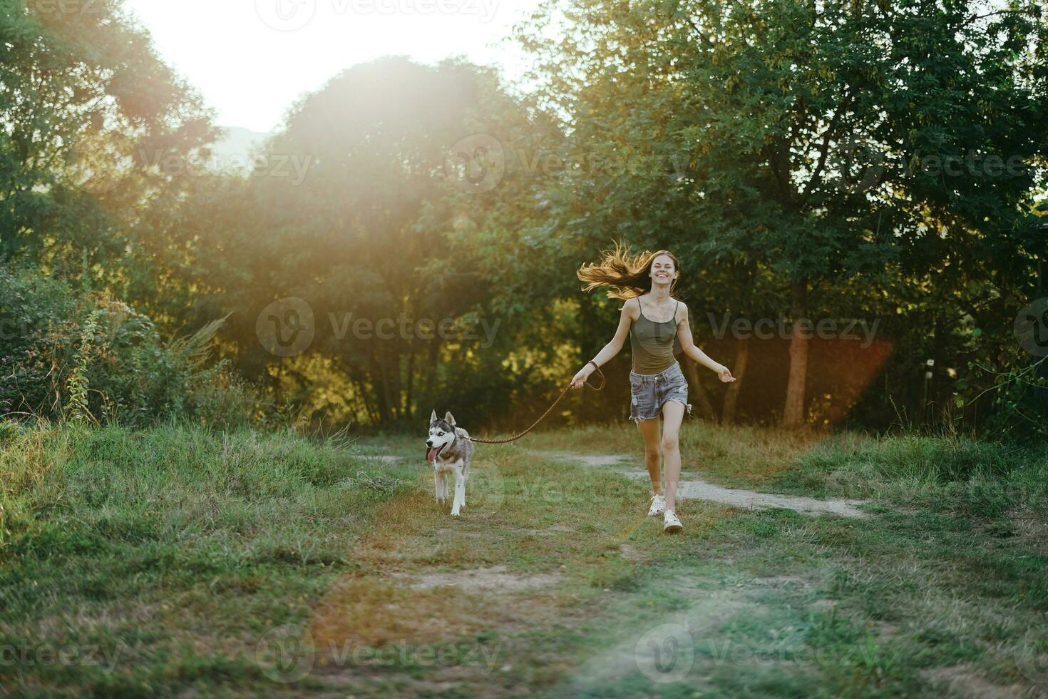 mulher e dela rouco cachorro alegremente corrida através a Relva dentro natureza dentro a parque sorrir com dentes outono andar com bicho de estimação, viajando com uma cachorro amigo foto