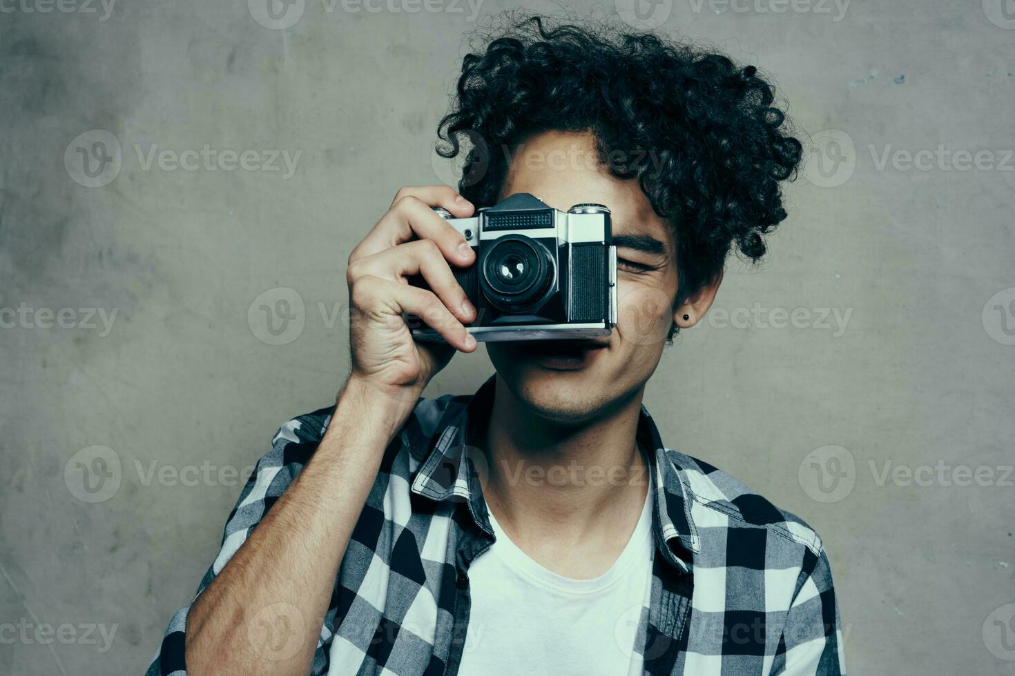 cara com uma Câmera dentro dele mãos em uma cinzento fundo dentro de casa passatempo xadrez camisa modelo foto