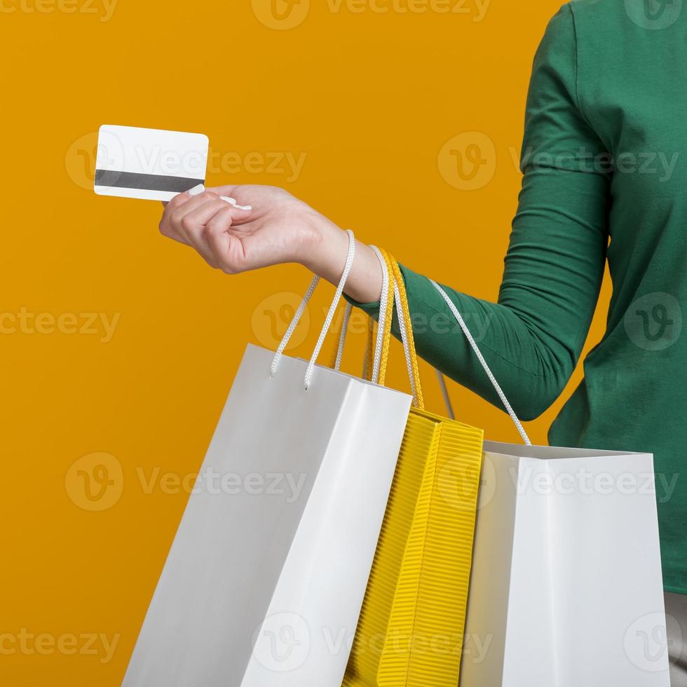 mulher segurando um cartão de crédito e muitas sacolas de compras em fundo laranja foto