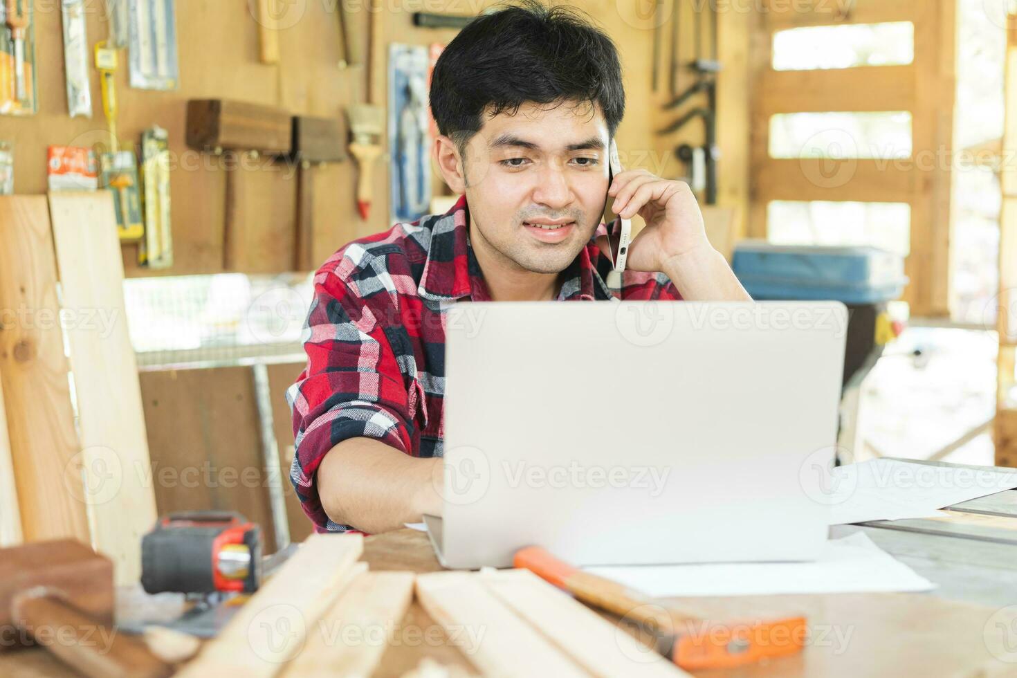 proprietário empreendedor comece pequeno fazer compras negócios. carpinteiro ásia jovem homem usando Smartphone, Móvel conversa com cliente sobre ordem, usar computador portátil computador para marketing on-line. fábrica indústria do madeira. foto