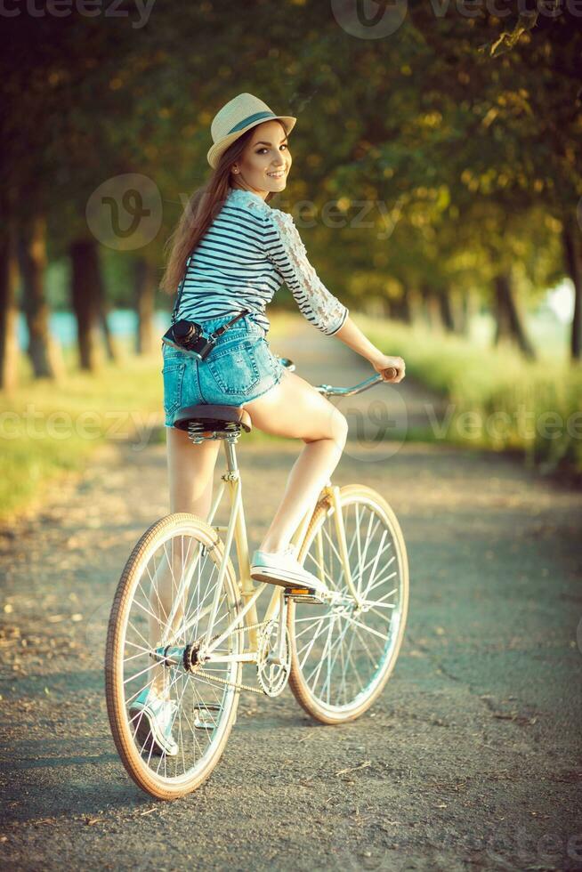 adorável jovem mulher dentro uma chapéu equitação uma bicicleta dentro uma parque foto