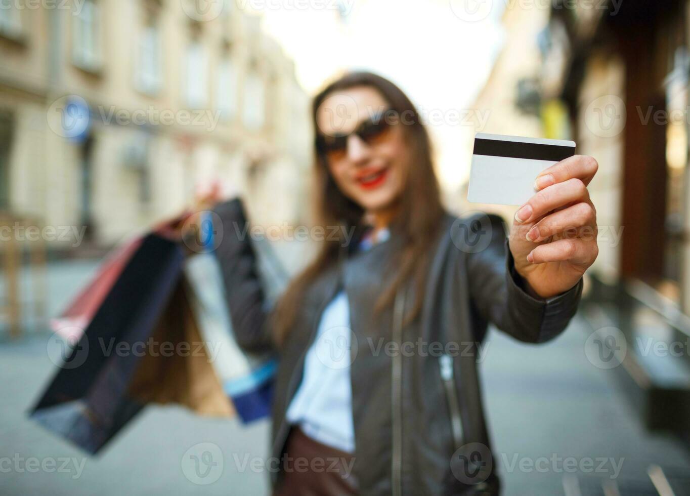 feliz lindo mulher com compras bolsas e crédito cartão dentro a mãos em uma rua foto