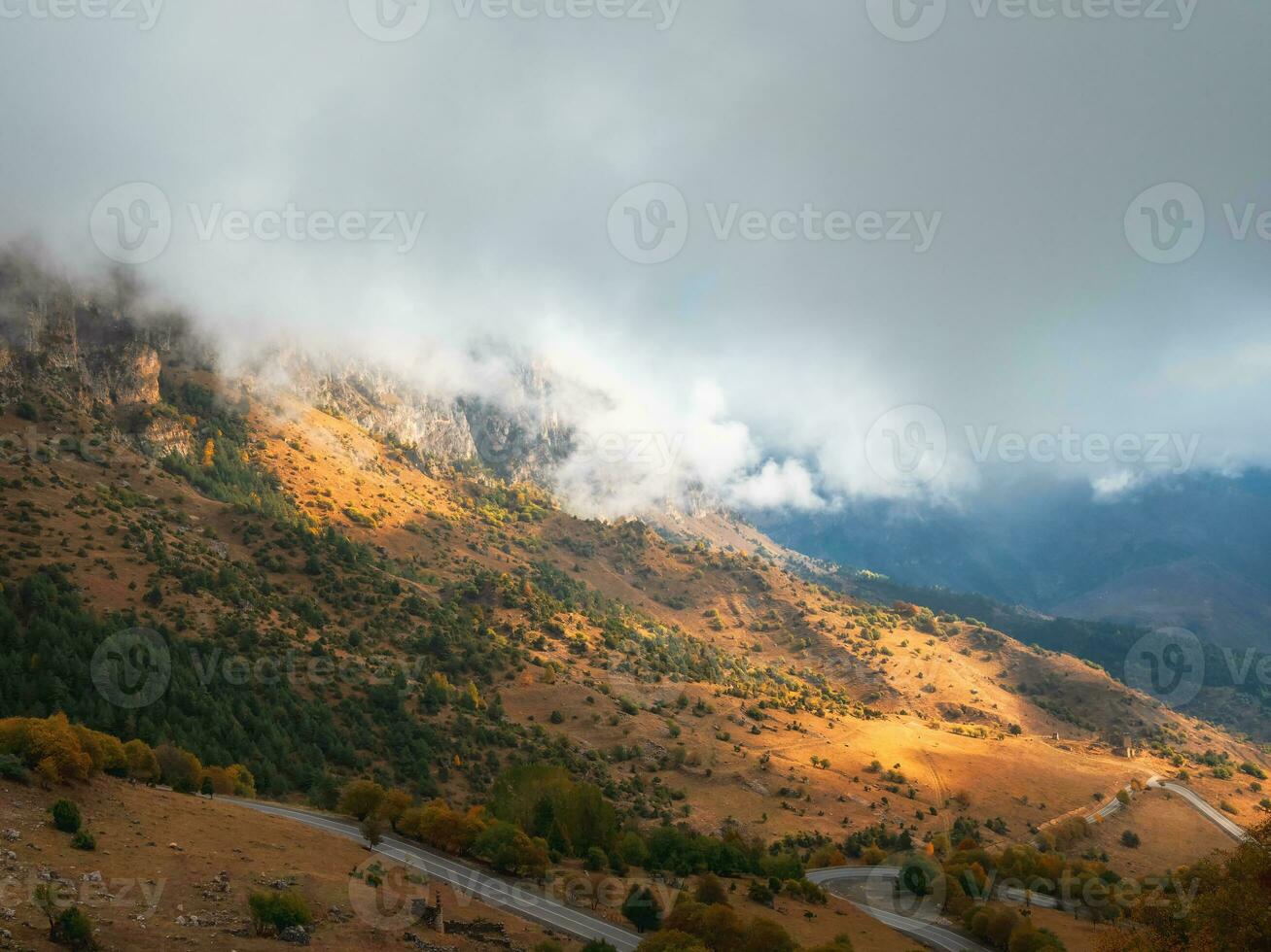 montanhas dentro uma denso névoa e ensolarado declive. místico panorama com lindo afiado pedras dentro baixo nuvens. lindo montanha nebuloso cenário em abismo Beira com afiado pedras. foto