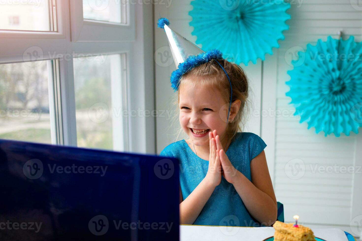 pequeno feliz menina aplausos dela mãos, comemora aniversário através da a Internet dentro quarentena tempo, auto-isolamento e família valores, conectados aniversário foto