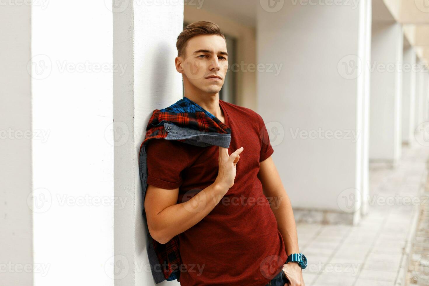 bonito jovem homem segurando uma camisa e em pé perto uma branco muro. foto
