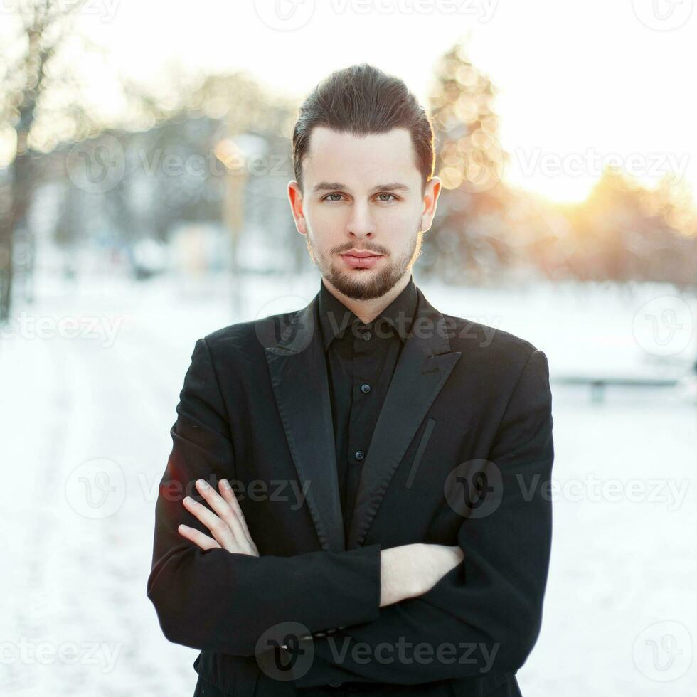 bonito jovem homem com uma barba vestindo uma Preto terno em uma pôr do sol foto