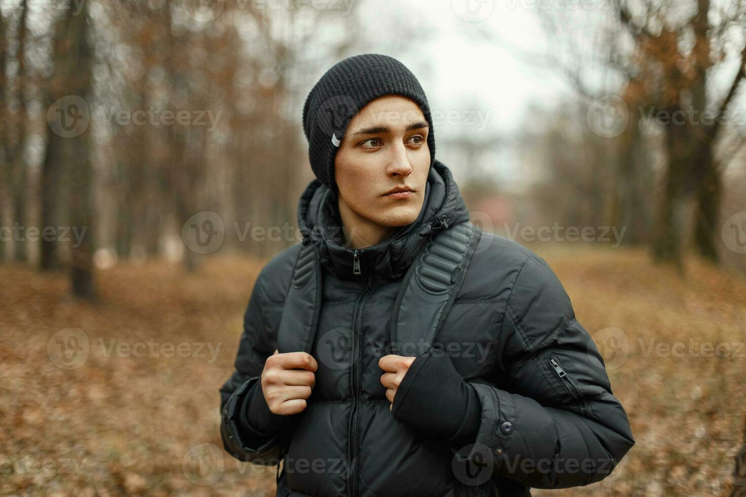 bonito à moda jovem homem dentro inverno Jaqueta e chapéu com mochila é viajando dentro a madeiras. foto