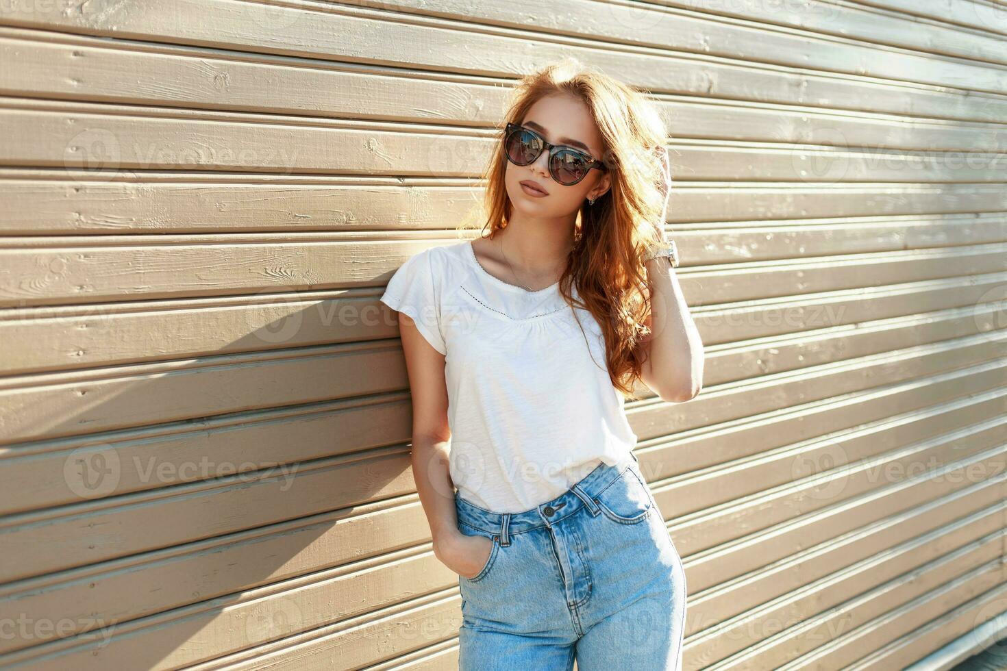 à moda bonita hipster mulher dentro oculos de sol e vintage Alto cintura jeans inclinou-se contra em a de madeira parede foto