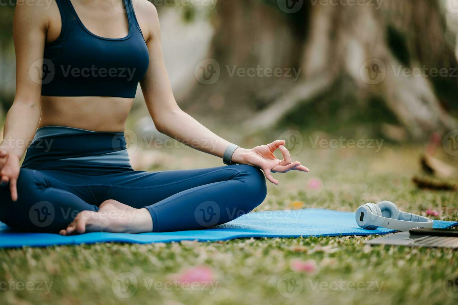 retrato do jovem mulher com fechadas olhos sentado dentro lótus posição em ioga esteira dentro a jardim. Sol luz foto