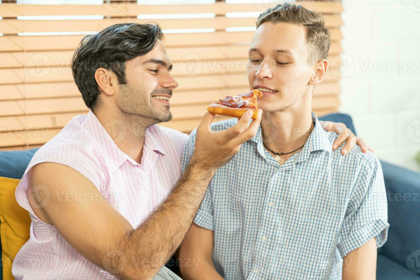 alegre gay casal comendo pizza. gay casal sentado em sofá às lar, comendo 1 fatia do pizza. homossexual relação conceito. foto