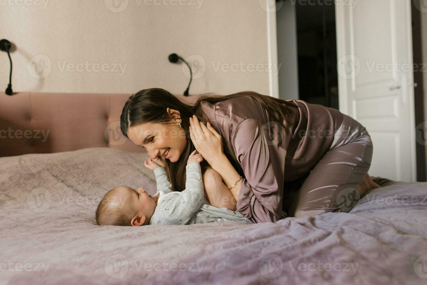 feliz mãe tendo Diversão e rindo com dela bebê em a cama foto