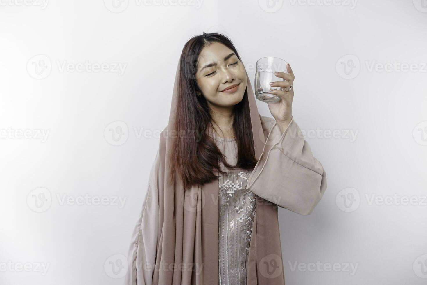 alegre ásia muçulmano mulher vestindo lenço de cabeça é bebendo uma vidro do água, isolado em branco fundo. foto