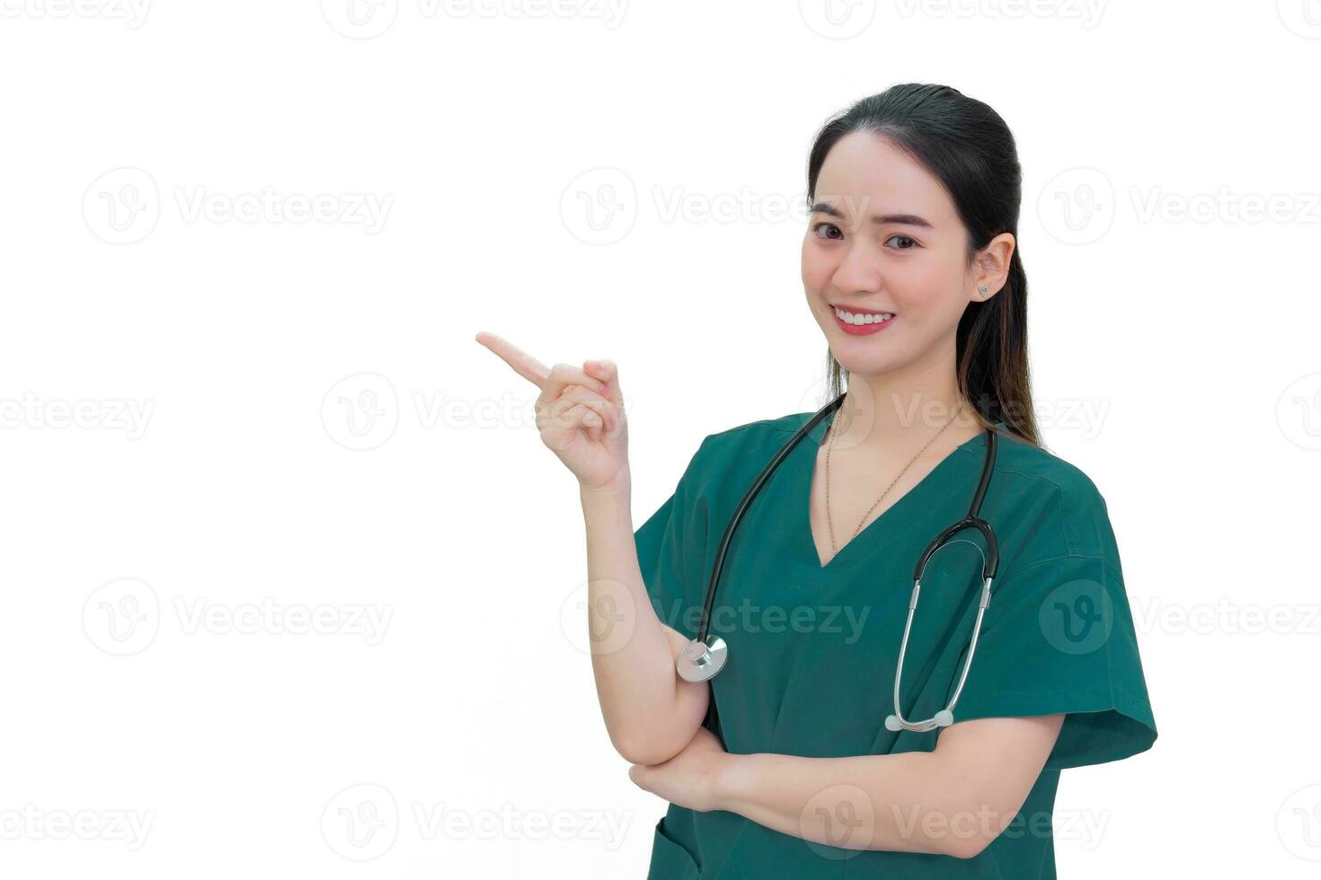 profissional ásia mulher médico dentro verde uniforme carrinhos e sorrisos enquanto apontando para a topo em branco fundo. foto