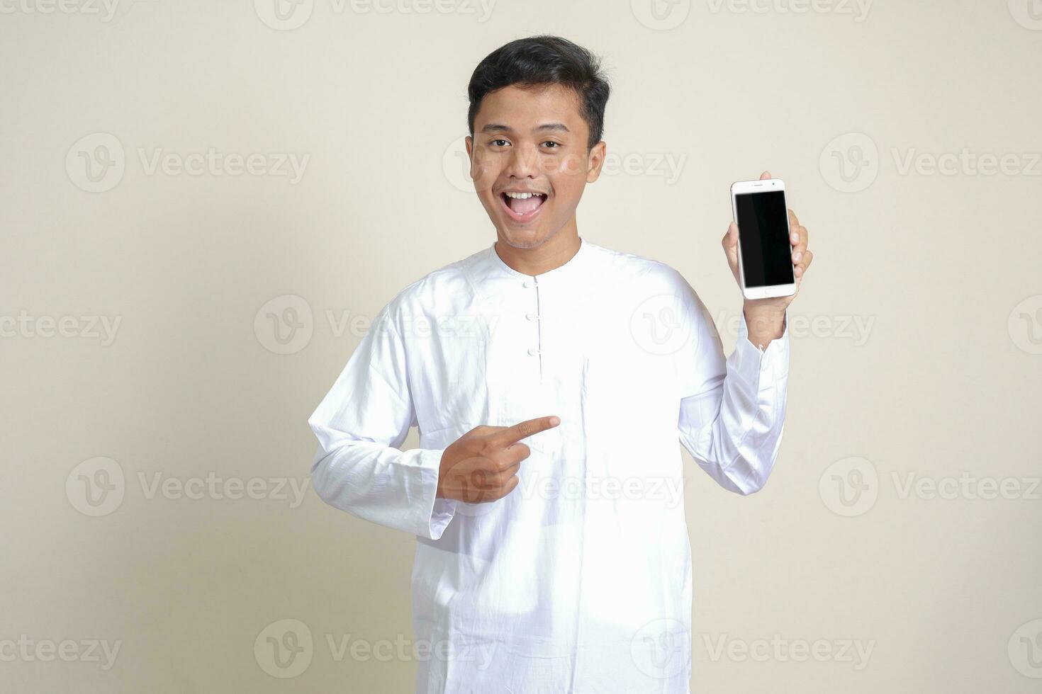 retrato do atraente ásia muçulmano homem dentro branco camisa mostrando e apresentando em branco tela Móvel telefone. publicidade conceito. isolado imagem em cinzento foto