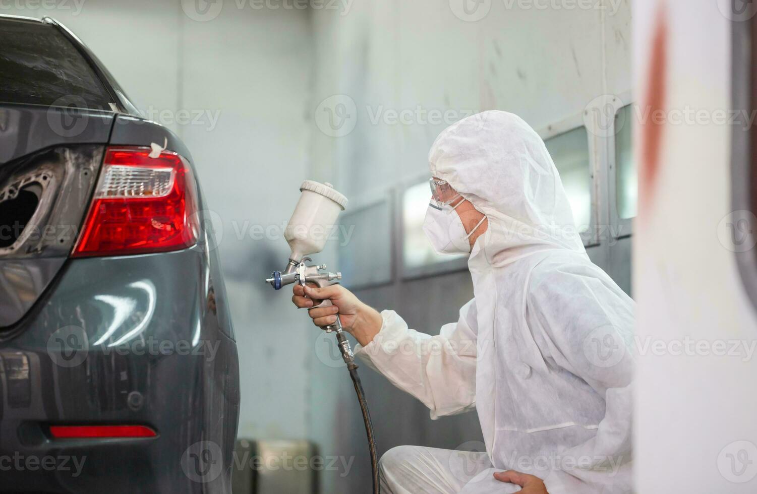 mecânico pintura carro dentro câmara. trabalhador usando spray arma de fogo e aerógrafo e pintura uma carro, garagem pintura carro serviço reparar e manutenção foto