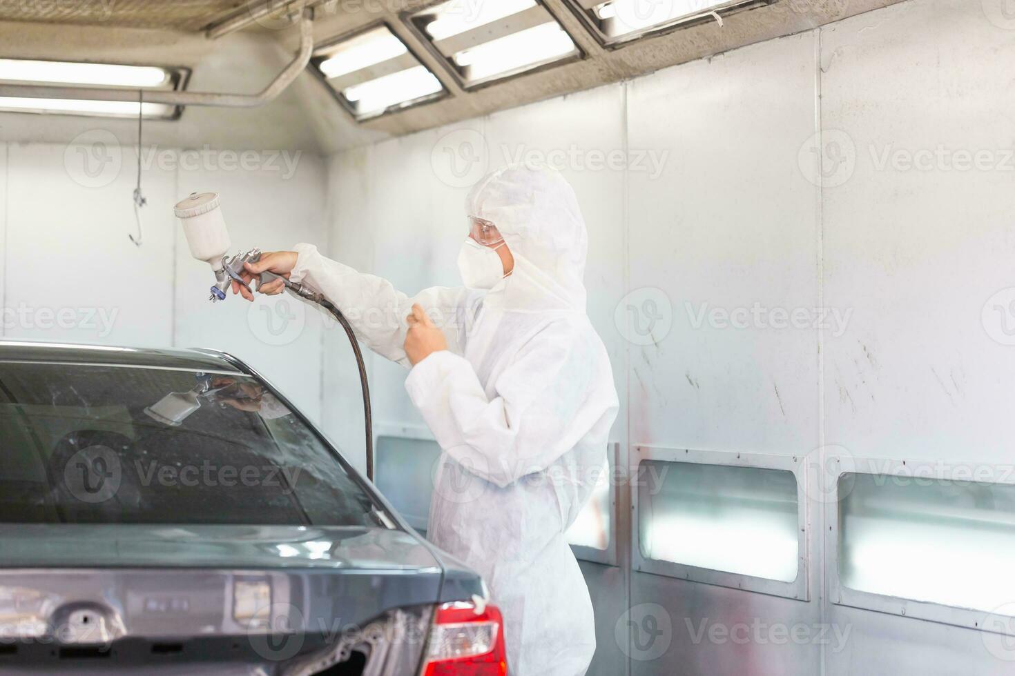 mecânico pintura carro dentro câmara. trabalhador usando spray arma de fogo e aerógrafo e pintura uma carro, garagem pintura carro serviço reparar e manutenção foto