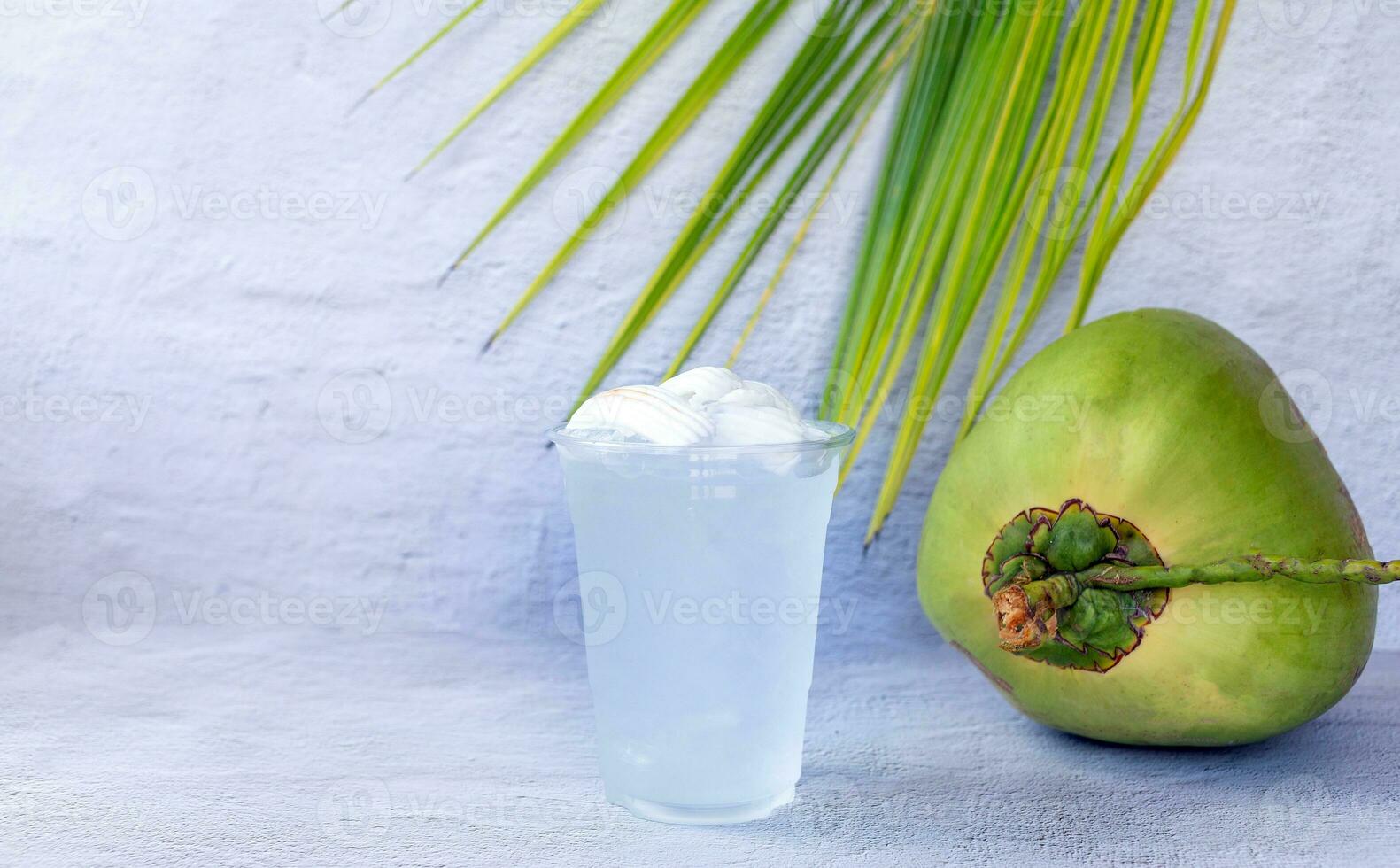 bebida de água de coco gelada em um copo de plástico e coco no fundo branco foto