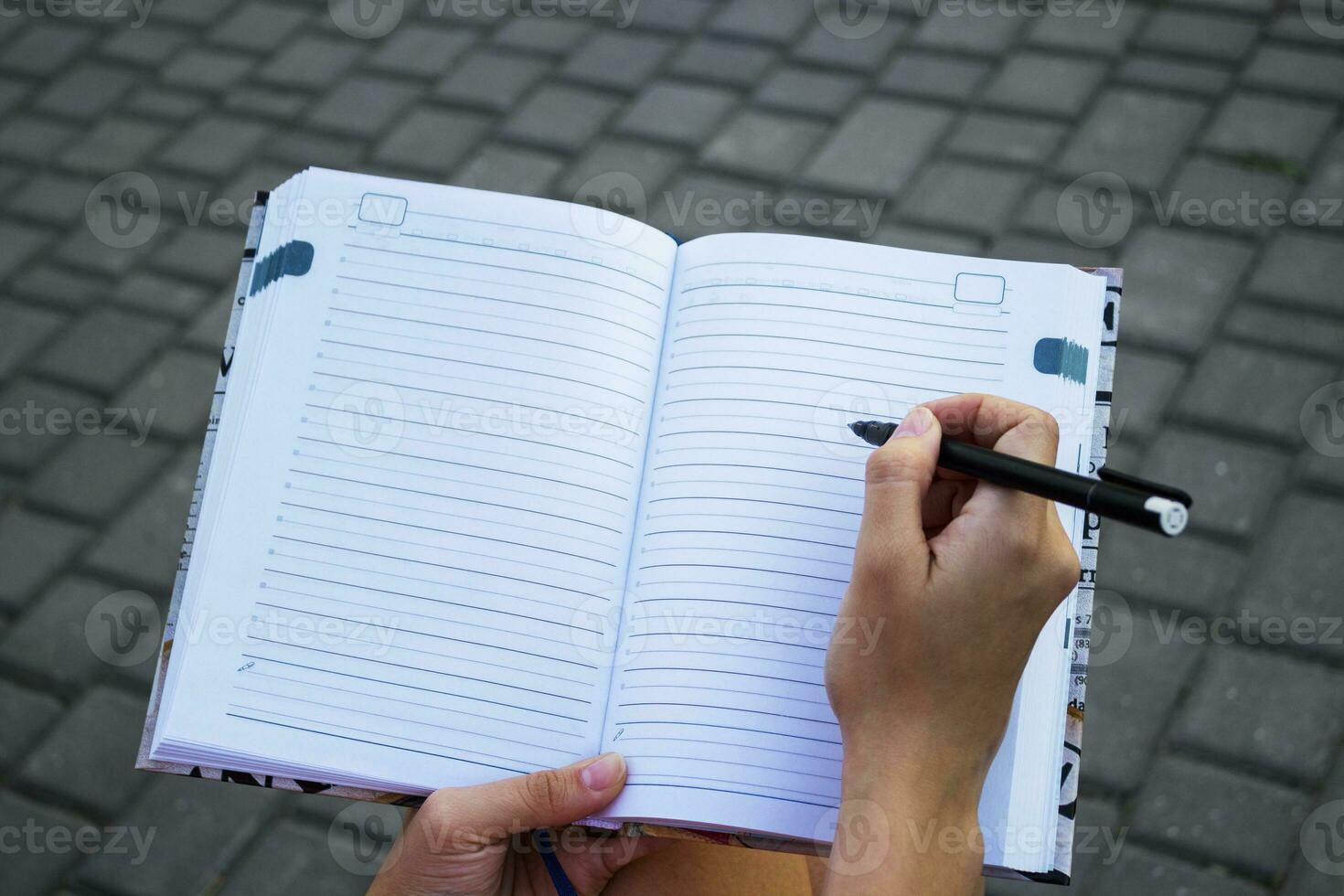 fechar-se do uma jovem menina escrevendo para dentro dela diário, dentro a parque foto