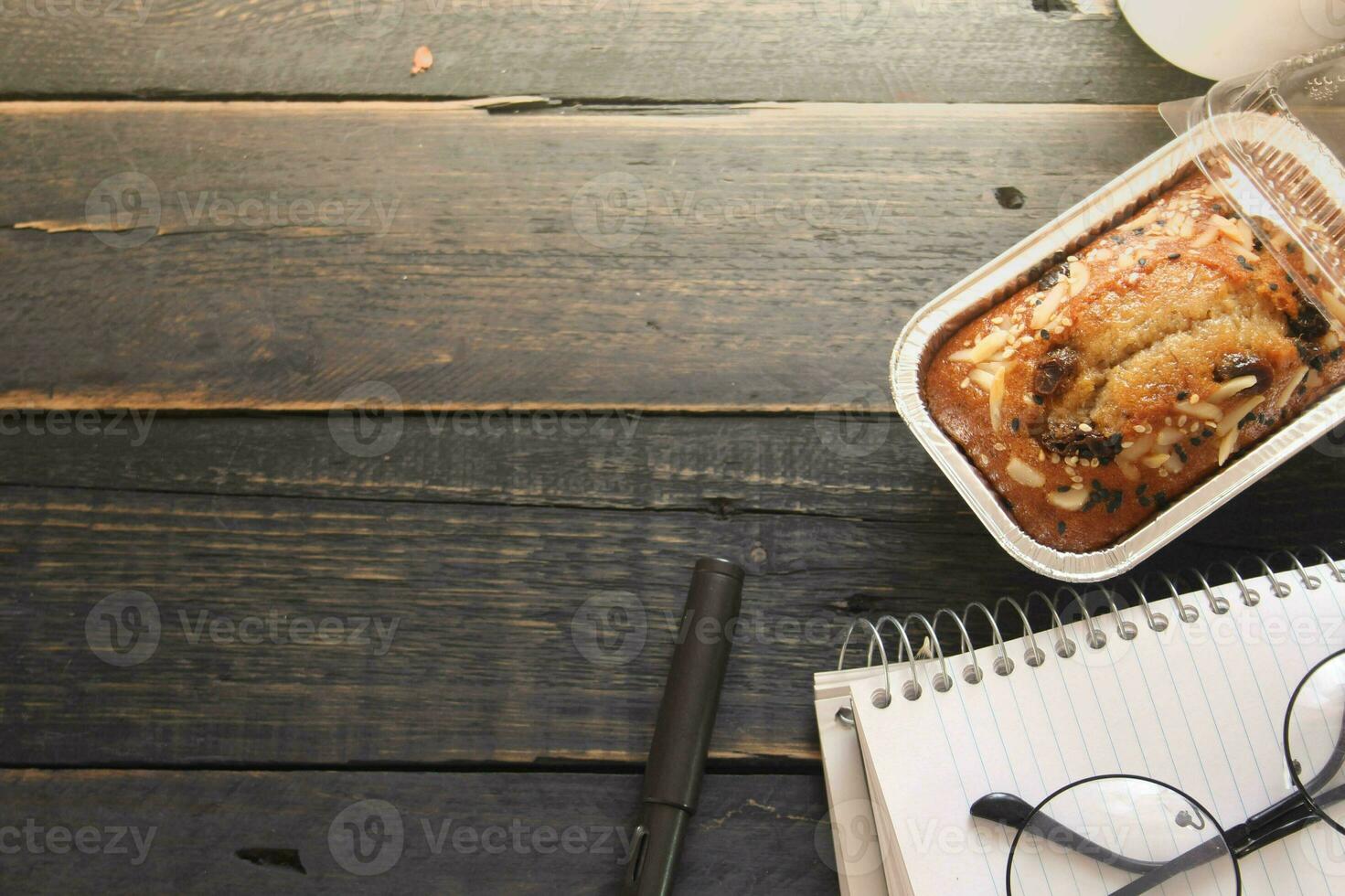 banana bolo em uma Preto de madeira mesa com Nota livro, copos, e café canecas. foto