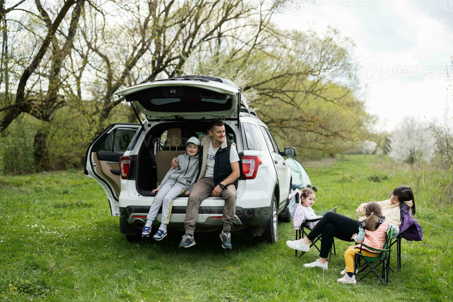 família com três crianças contra carro aberto tronco em piquenique. foto