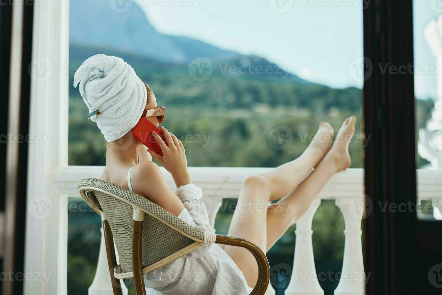 atraente jovem mulher dentro oculos de sol senta em a sacada e usa a telefone perfeito ensolarado manhã foto