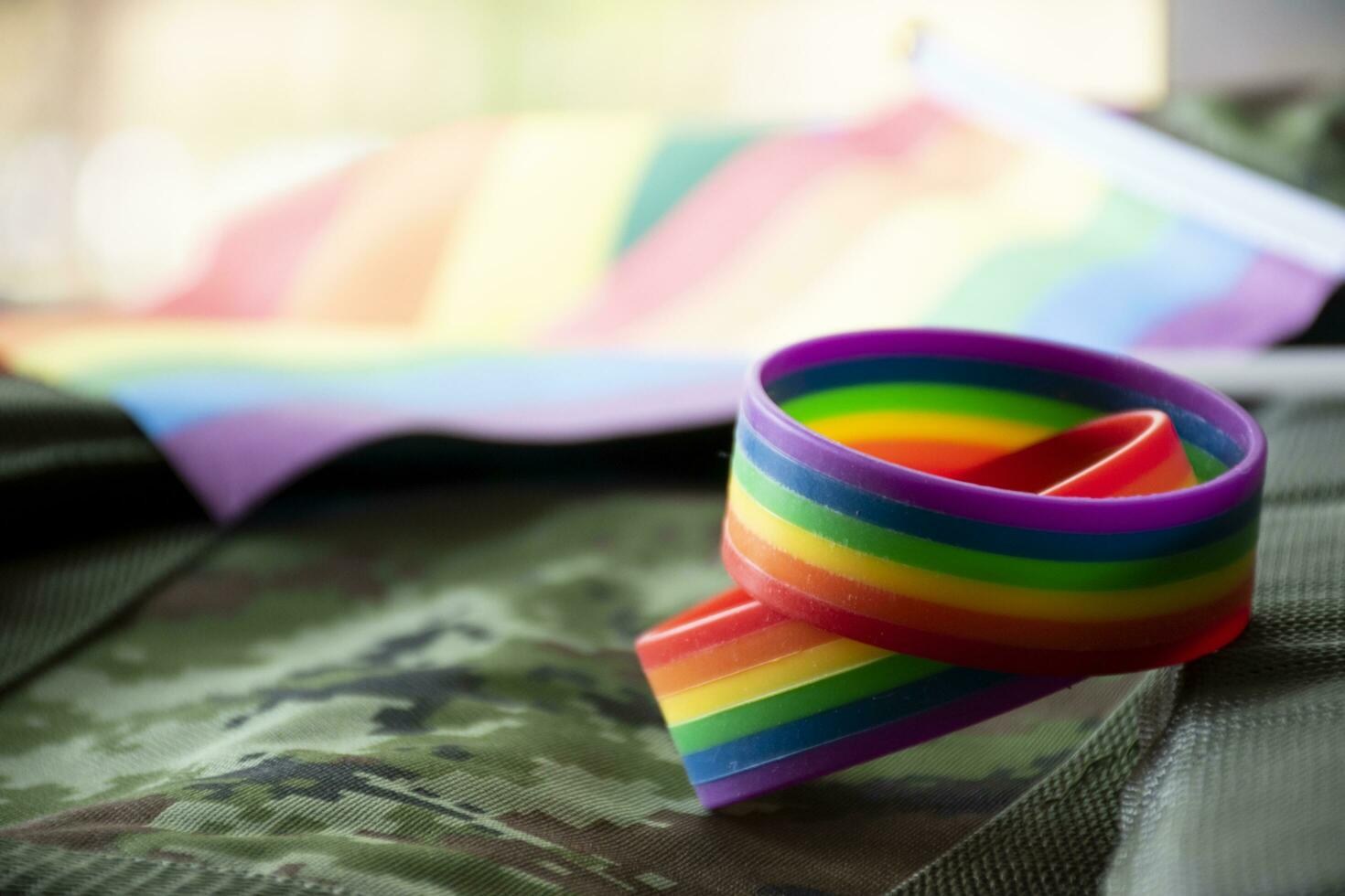 arco Iris bandeira e arco Iris pulseiras em camuflar fundo, conceito para celebrações do lgbt pessoas dentro orgulho mês por aí a mundo, suave e seletivo foco em pulseira. foto