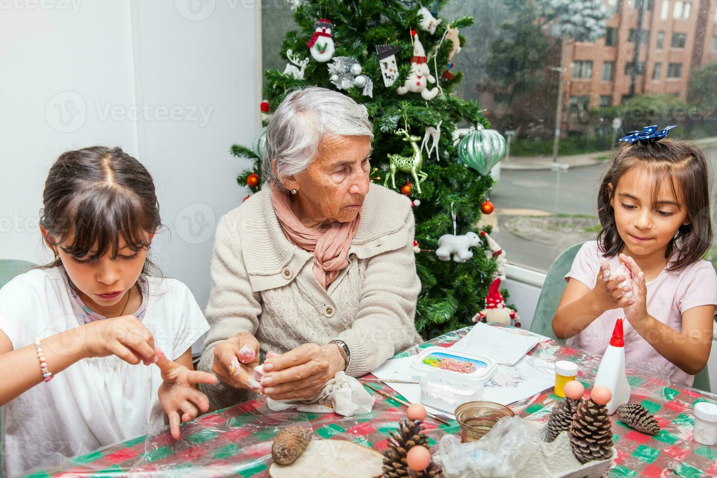 pequeno meninas tendo Diversão enquanto fazer Natal natividade trabalhos manuais com seus avó - real família foto