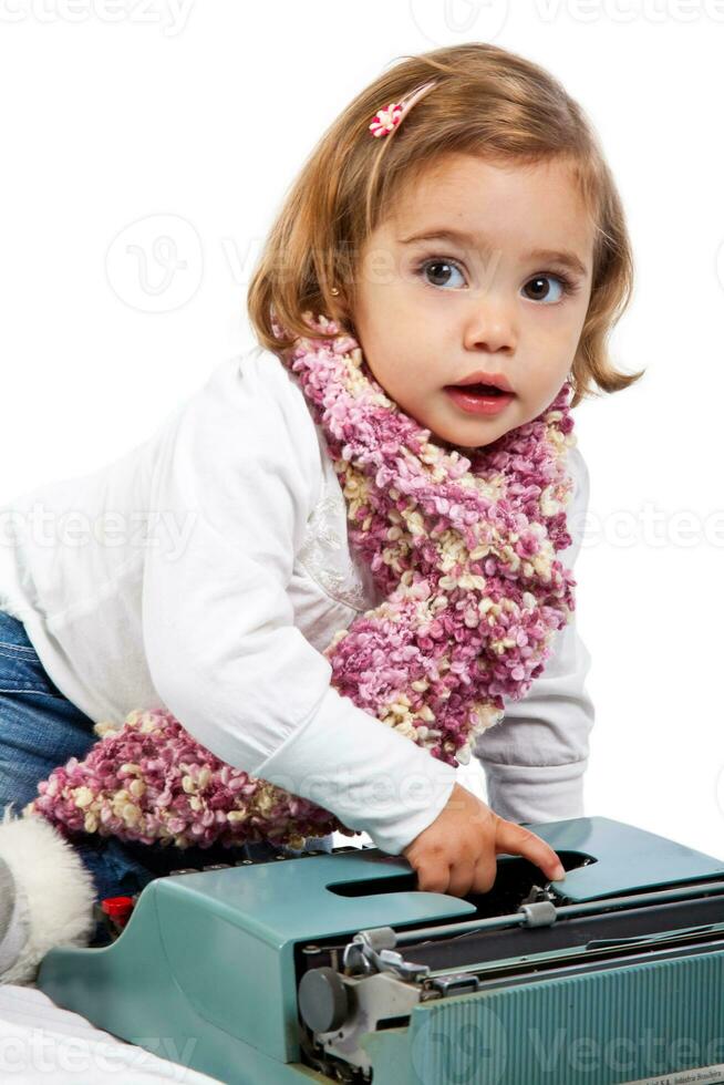 lindo pequeno Loiras menina jogando com uma máquina de escrever foto