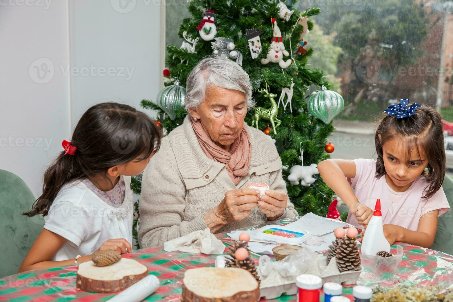 pequeno meninas tendo Diversão enquanto fazer Natal natividade trabalhos manuais com seus avó - real família foto