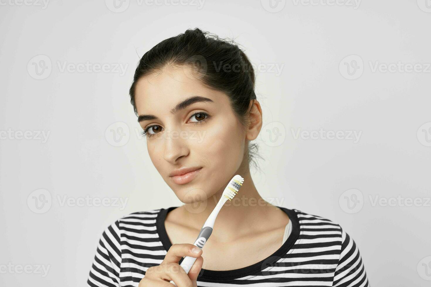 mulher dentro uma listrado camiseta escova de dente dentro mão luz fundo foto