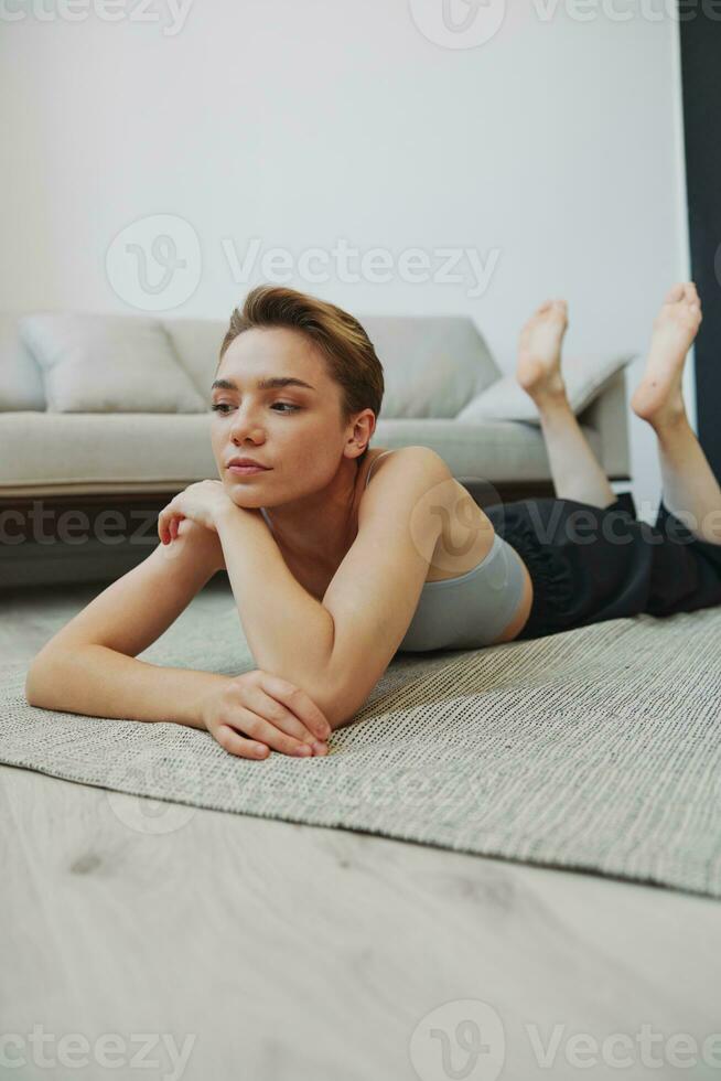 Adolescência menina deitado em a chão às casa sorridente dentro casa roupas com uma curto corte de cabelo, estilo de vida sem filtros, livre cópia de espaço foto