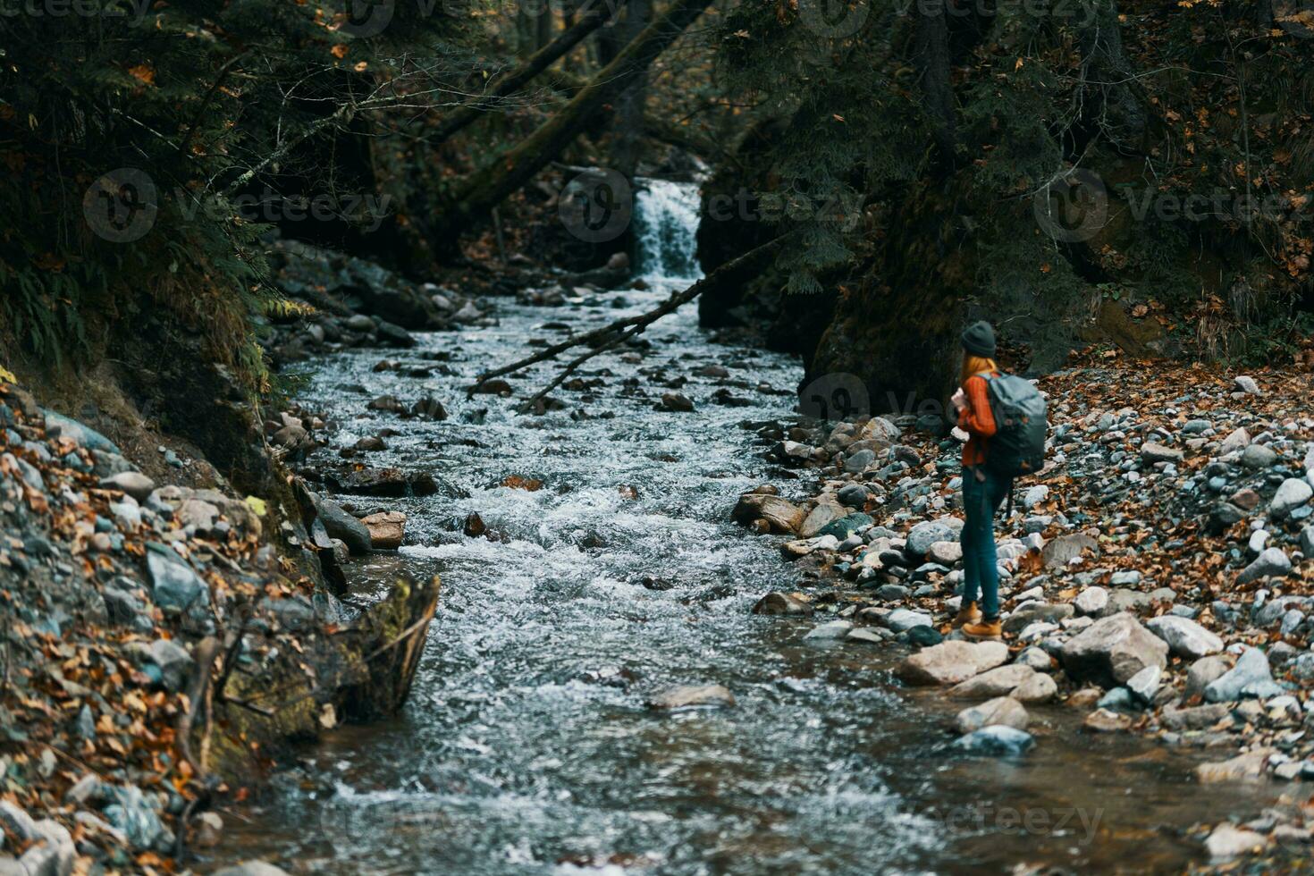 mulher caminhante com uma mochila em a rio banco e a floresta dentro a distância alta árvores foto