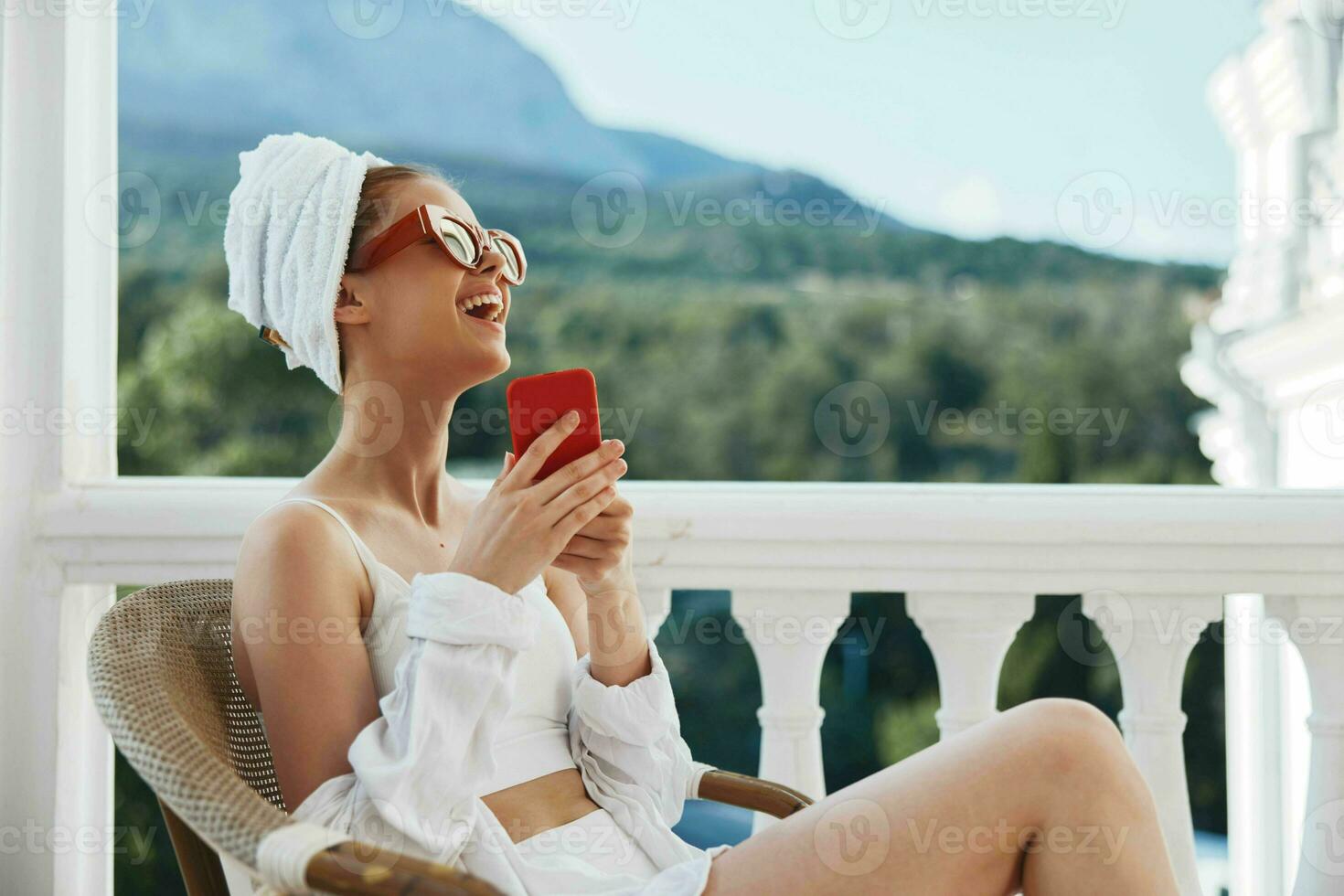 lindo mulher dentro uma branco camisa senta em a sacada com uma telefone preguiçoso manhã foto