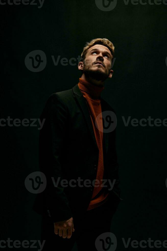 elegante homem dentro Jaqueta e suéter olhando acima contra uma Sombrio fundo foto