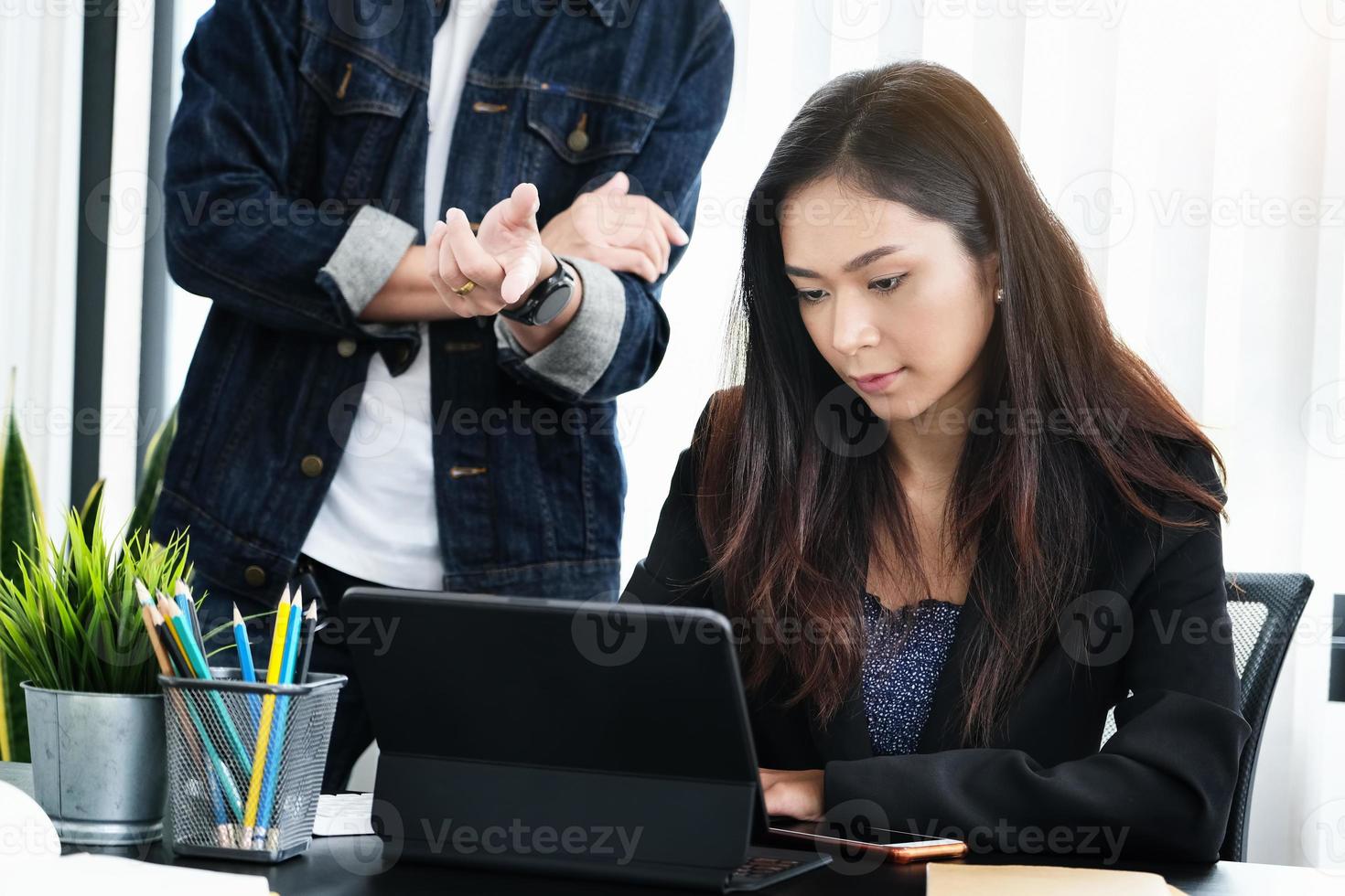 mulher trabalhando em um tablet com um homem falando atrás dela foto