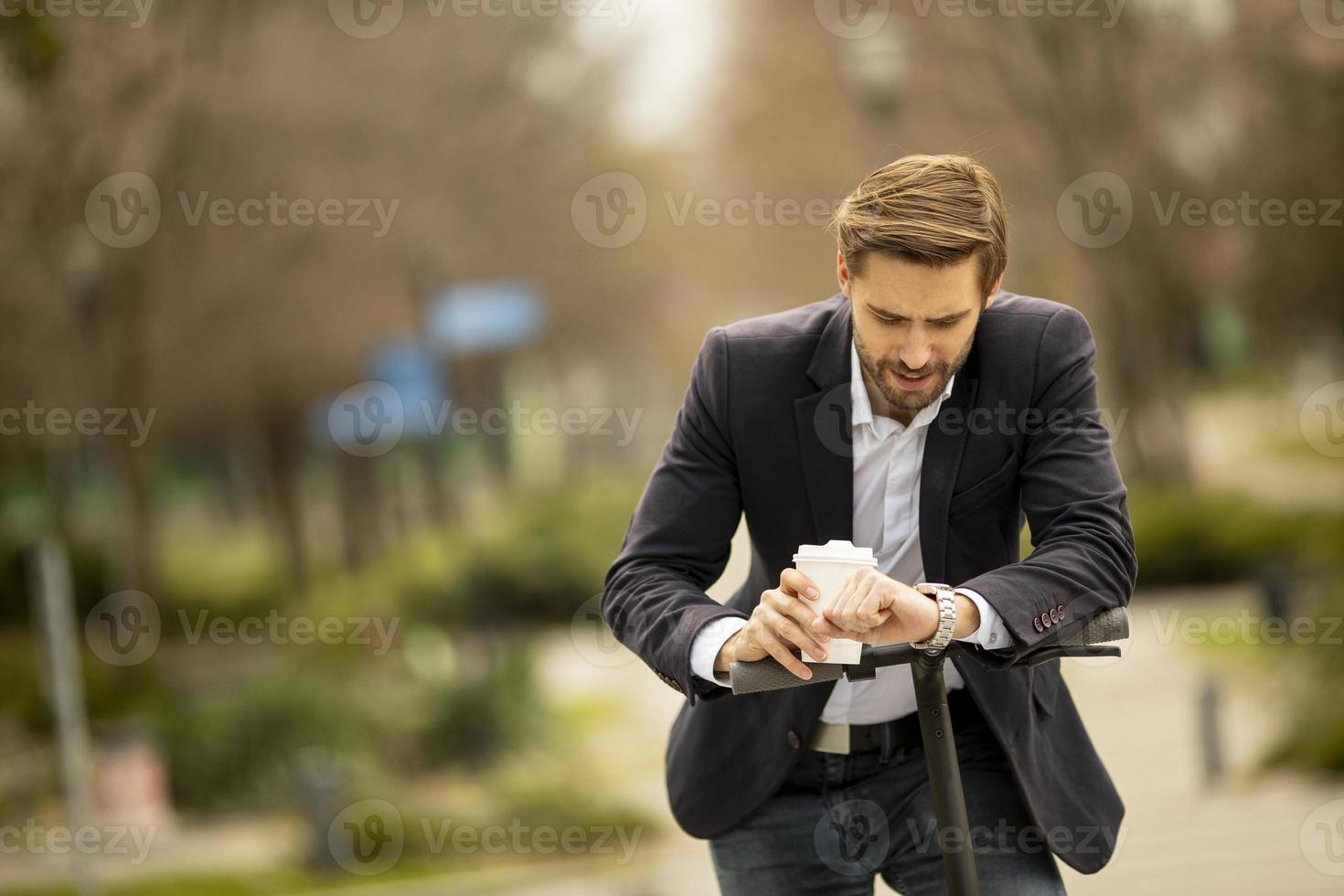 empresário com xícara de café verificando o tempo na scooter elétrica foto