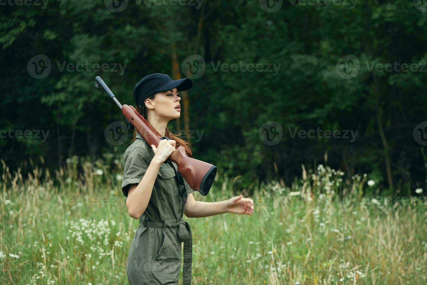 mulher em natureza a arma de fogo em a ombro verde macacão Preto boné verde folhas foto