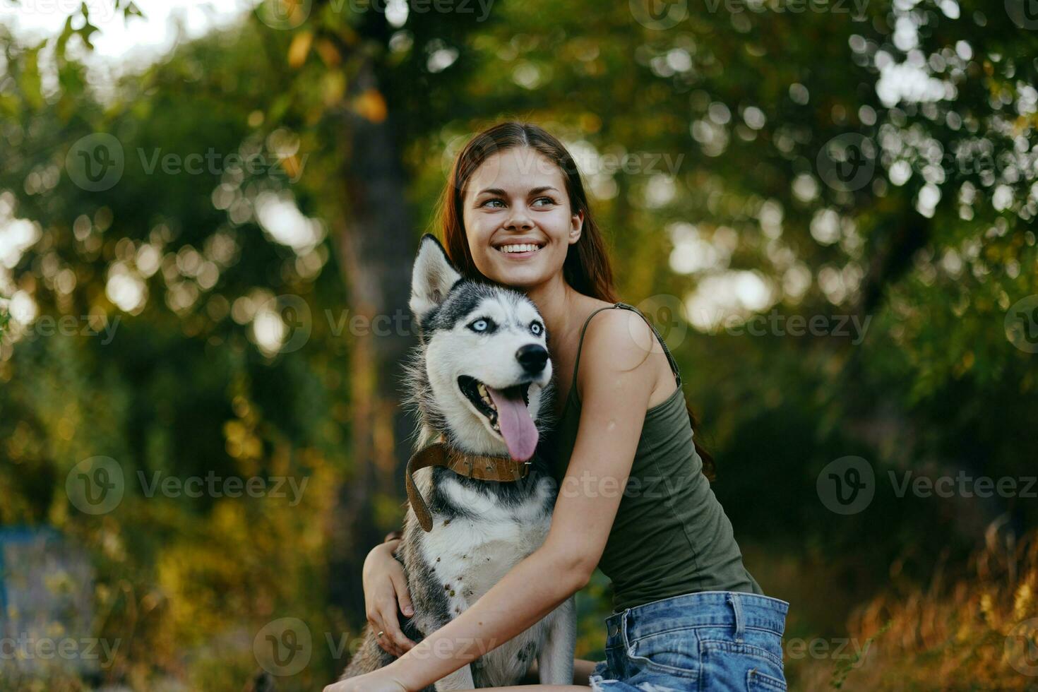 alegre mulher com uma rouco procriar cachorro sorrisos enquanto sentado dentro natureza em uma andar com uma cachorro em uma trela outono panorama em a fundo. estilo de vida dentro anda em com animais de estimação foto